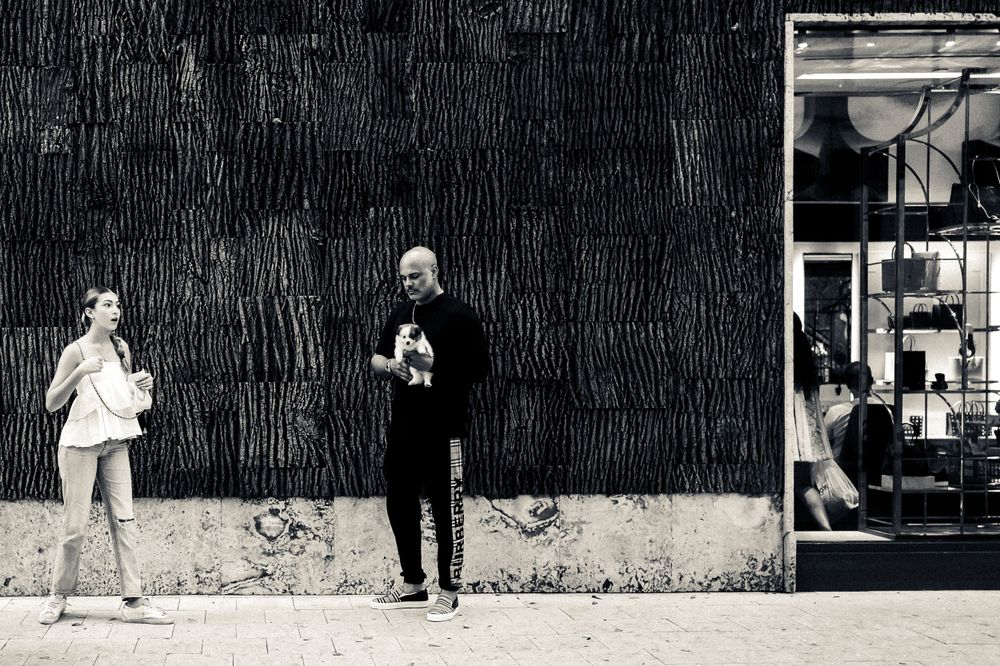 Street scene with people standing against textured wall in black and white photography.