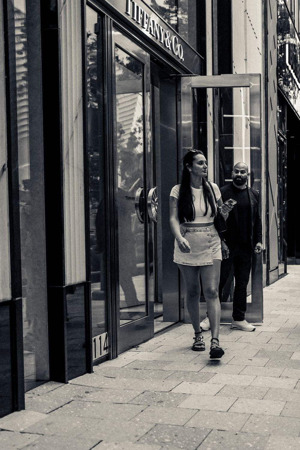 Street scene outside high-end retail stores with pedestrians walking on sidewalk.