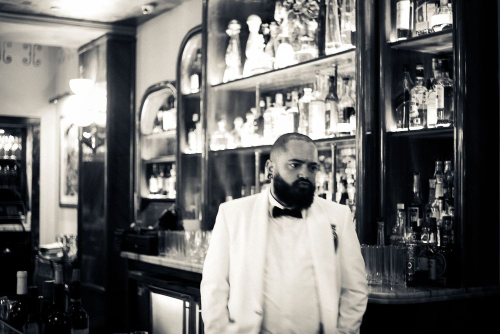 Black and white view of a bar interior with bottles displayed on shelves.