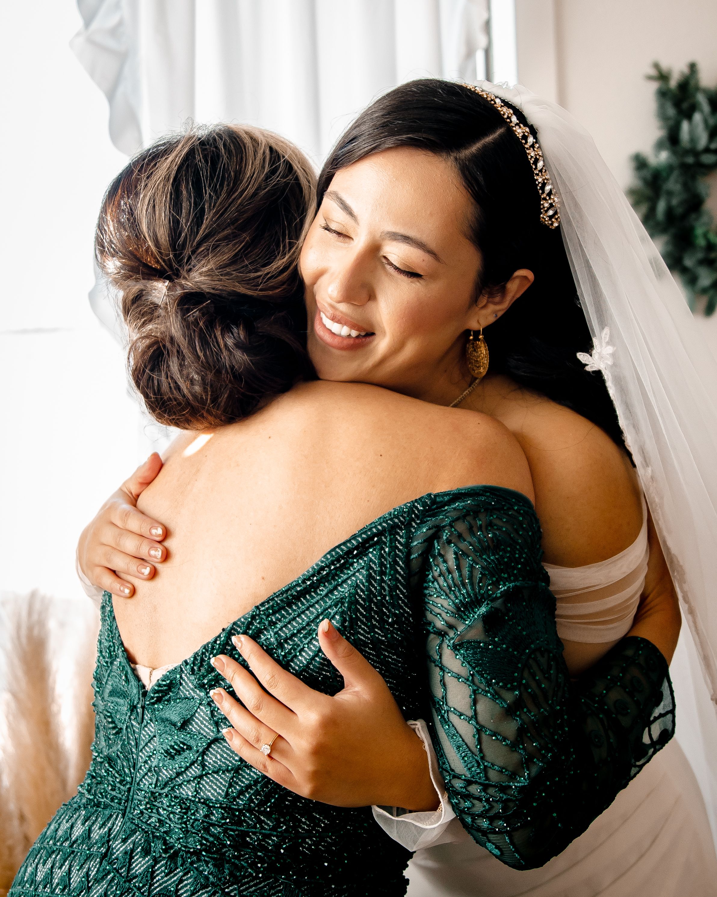 Two people share an emotional embrace in a white room while wearing emerald green formal attire.