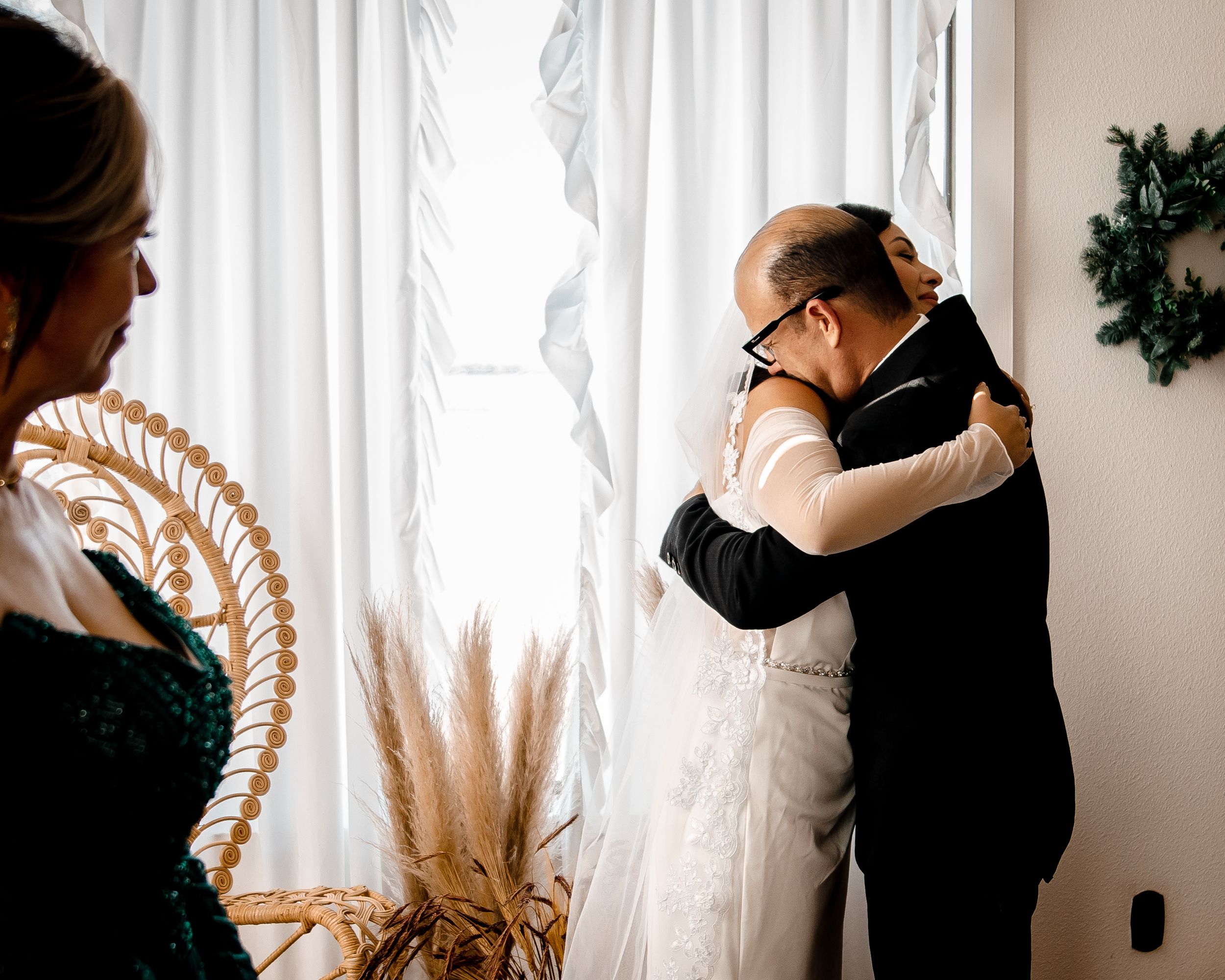 A romantic couple embraces in front of white curtains with dried pampas grass creating an ethereal atmosphere.