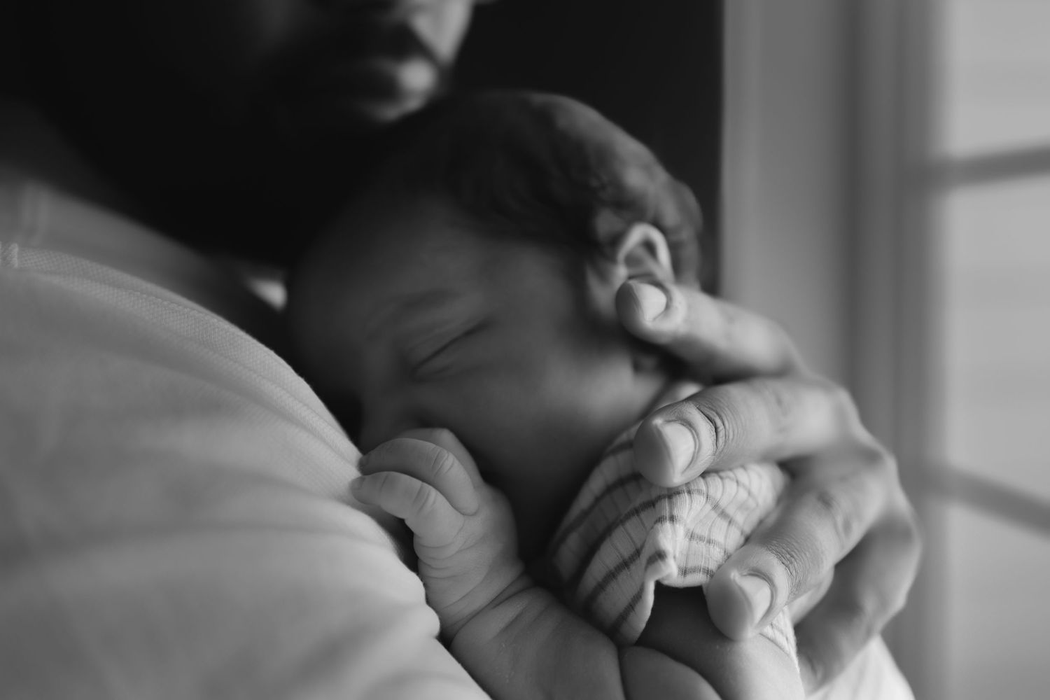 close up back and white image of a sleeping newborn on a mans chest, his hand on newborns back