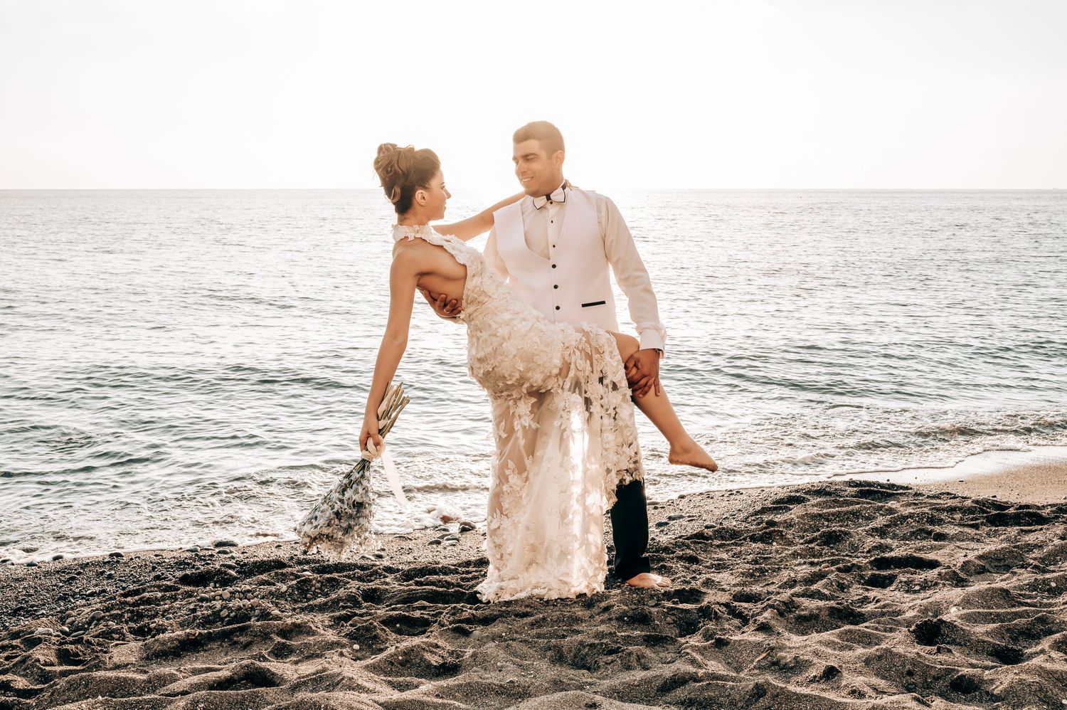 Couple in wedding attire sharing an intimate pose on a beach at sunset.