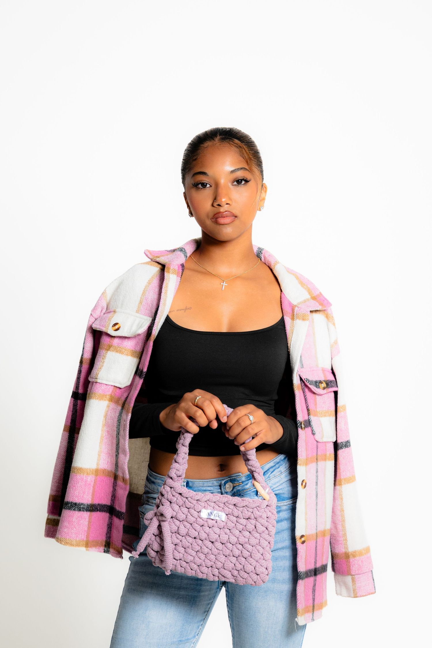 Fashion model wearing pink plaid jacket and holding purple knit handbag.