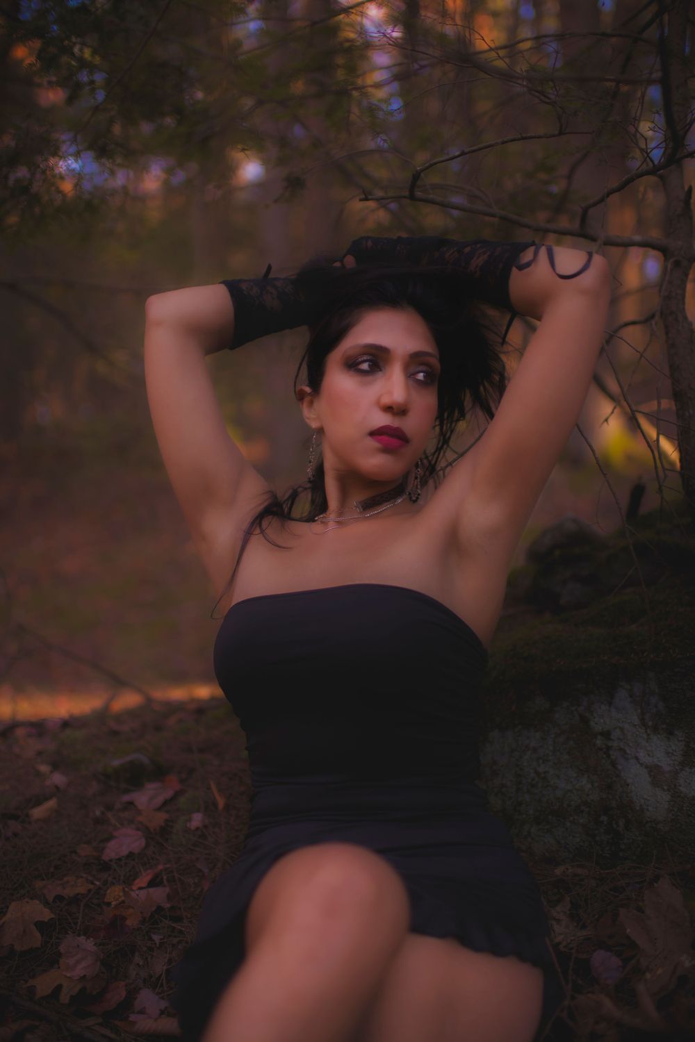 Dramatic portrait in black dress against sunlit autumn forest background.