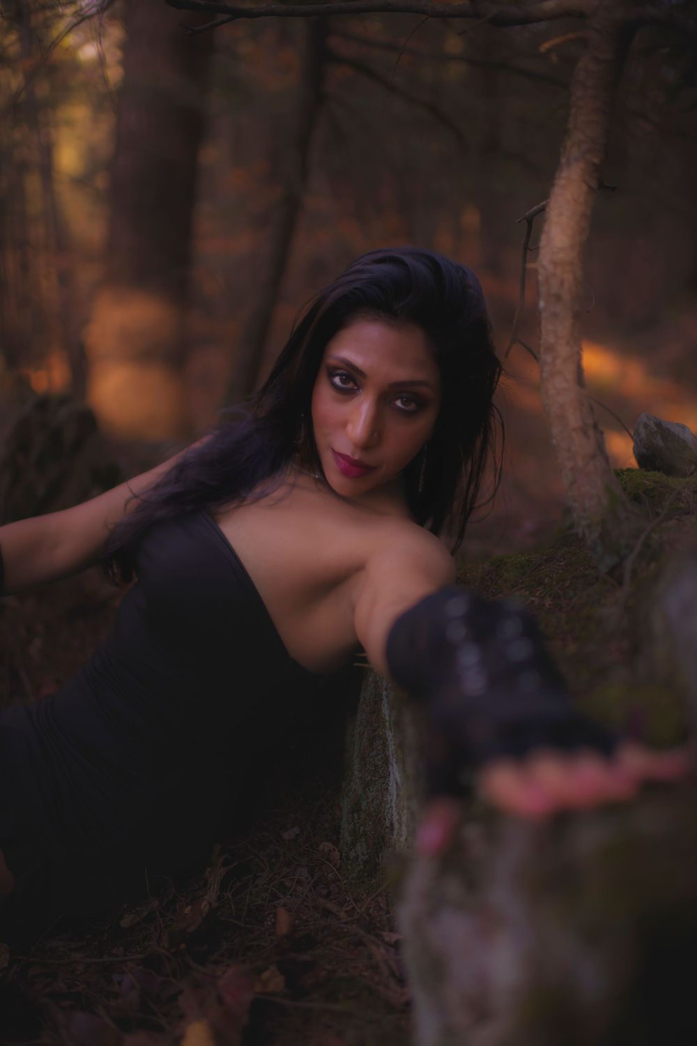 A moody portrait in a dark forest with dramatic lighting and a black dress.