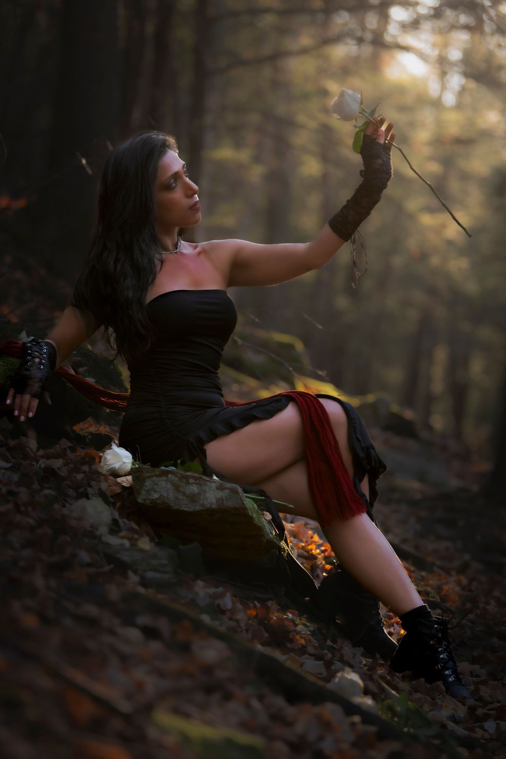 Forest fashion shoot with black dress and red accents among autumn leaves.