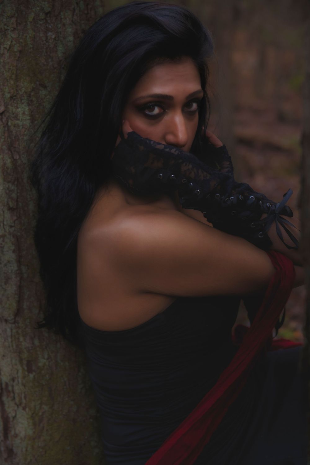 Dark fashion photography in a forest setting with black and red styling elements.