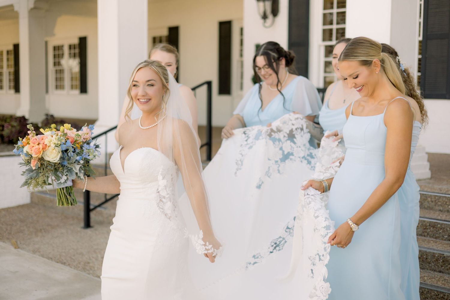 Three people in wedding attire walking together outside a white columned building.