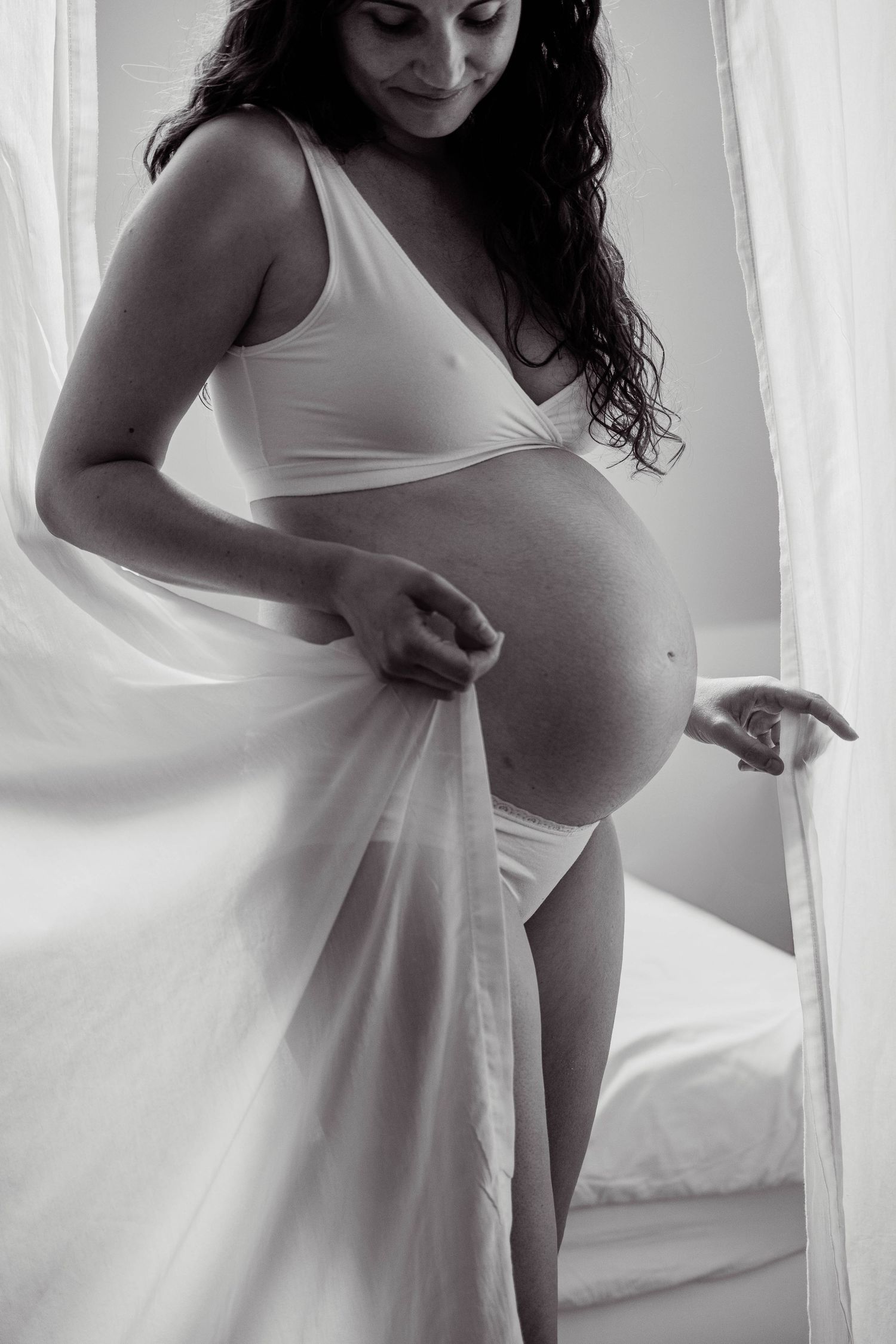 Black and white maternity portrait of woman in lace dress standing in field with flowers.