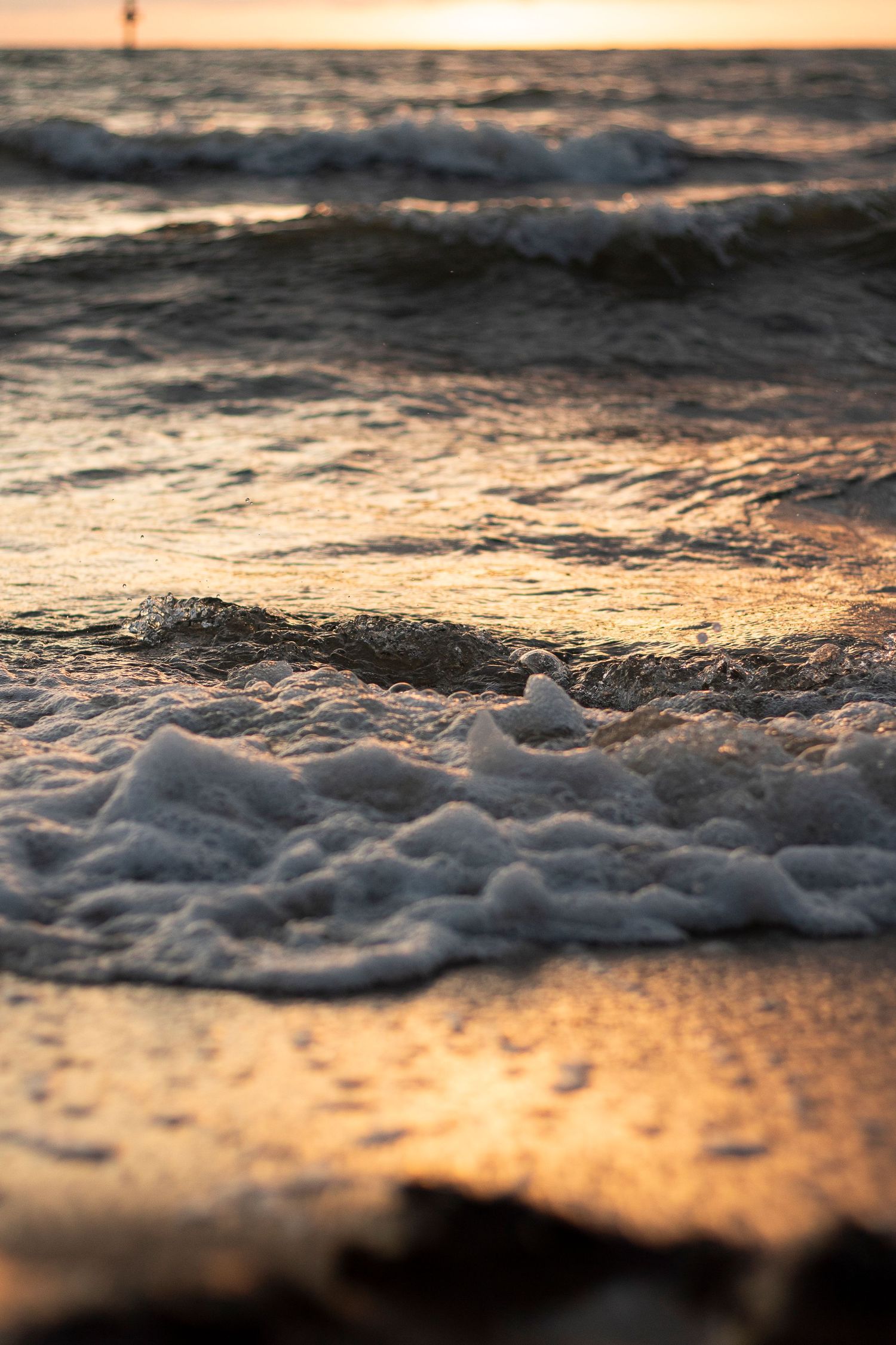Close-up of ocean waves breaking on shore during golden sunset with bokeh effect.