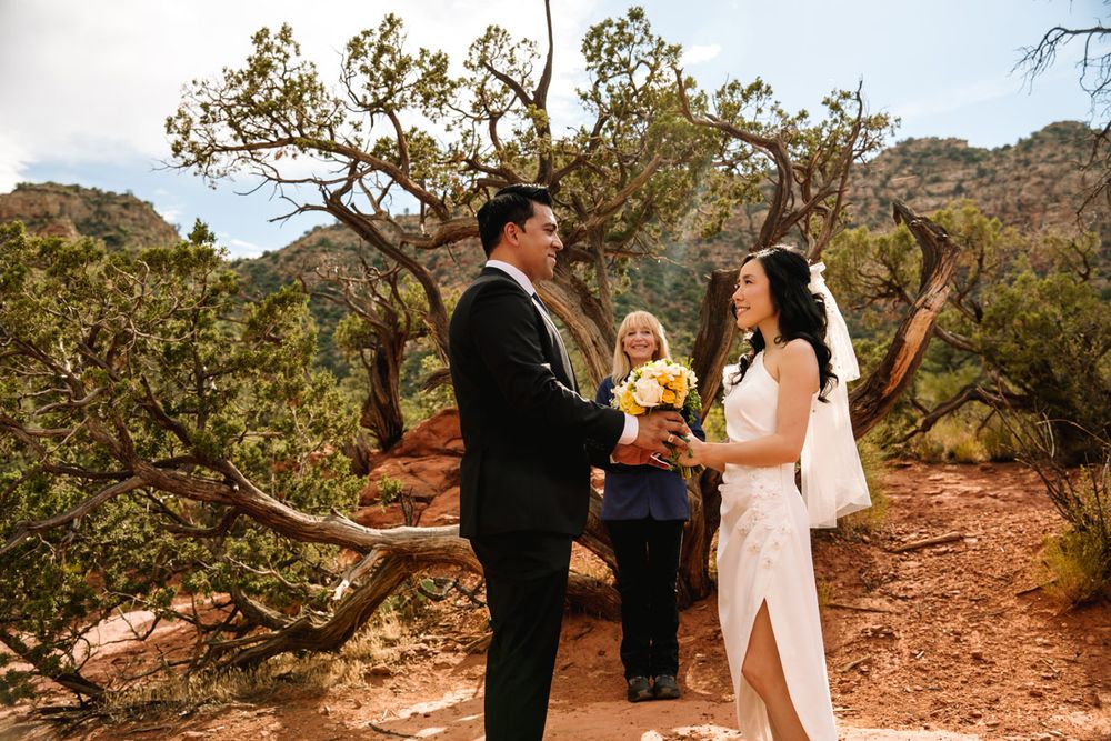 An intimate outdoor wedding ceremony takes place among Sedona desert trees with mountain views.