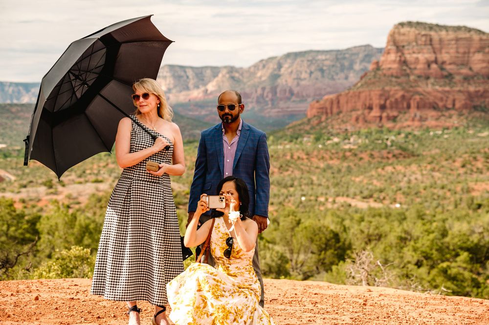 Three people pose with umbrellas against a dramatic Sedona red rock canyon landscape.