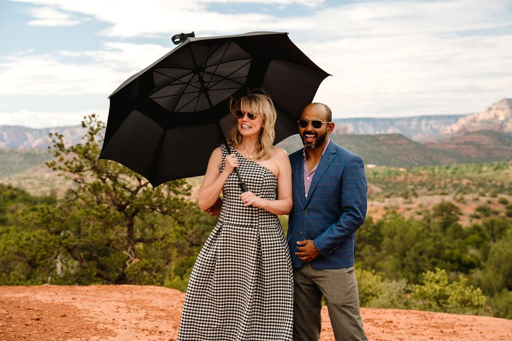 A couple poses with a black umbrella against a backdrop of scenic Sedona red rock mountains.