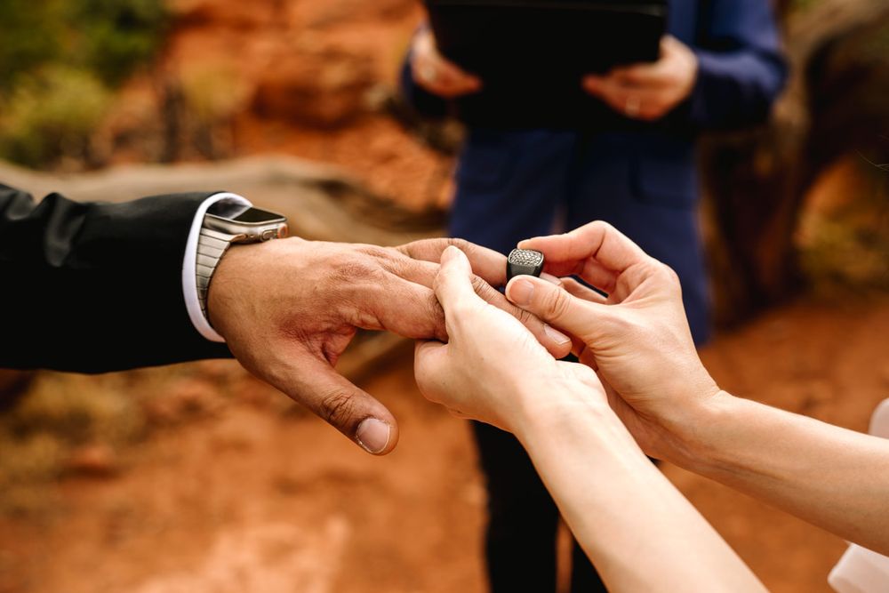 Close-up of hands exchanging wedding rings during an outdoor ceremony on Sedona red rocks.