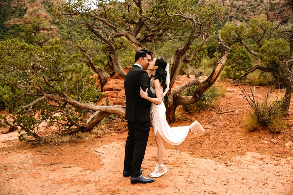 A couple shares a playful dance moment on a rustic trail with Sedona's red rocks in the background.