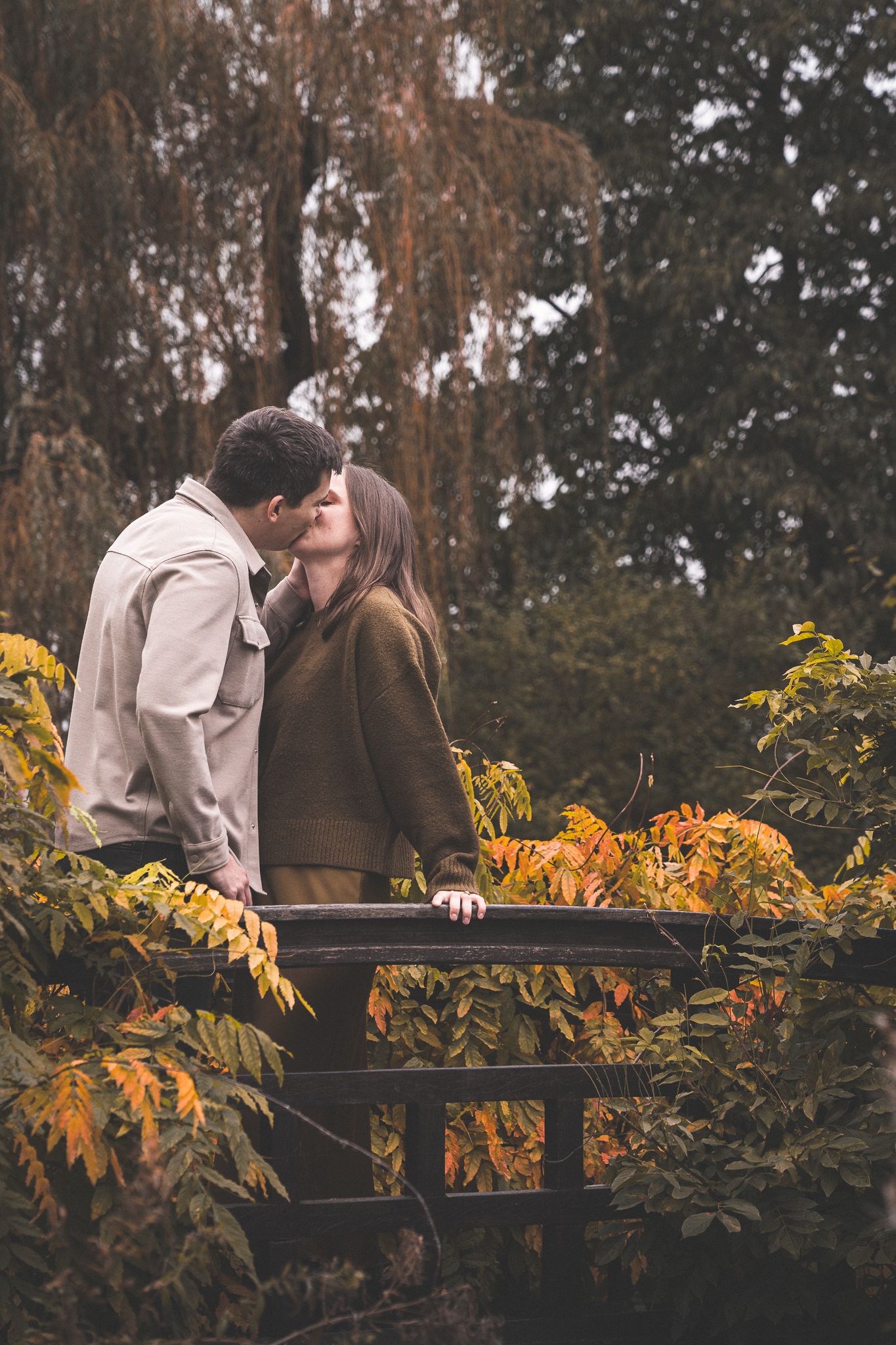 Romantic couple poses by autumn foliage and railing.