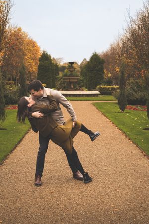A playful couple performs a romantic dance dip sequence on a garden pathway in autumn.