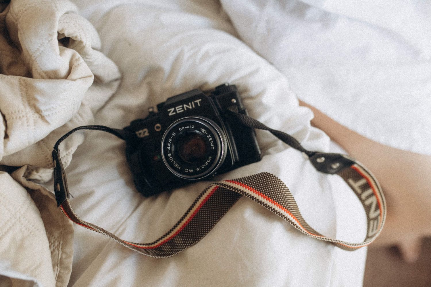 Vintage Zenit camera with brown leather strap lying on white bedding.