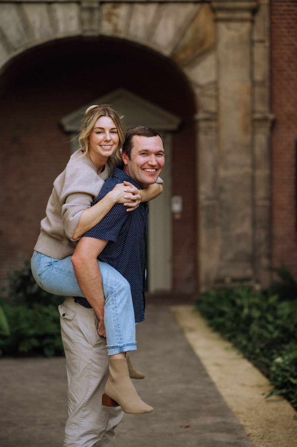 Playful couple sharing a piggyback ride under historic brick archways.