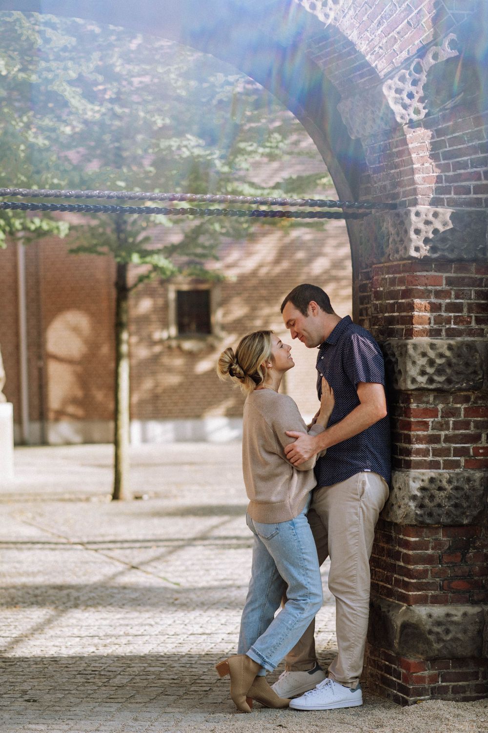 Romantic moment captured under brick archways with warm lighting and cobblestone ground.