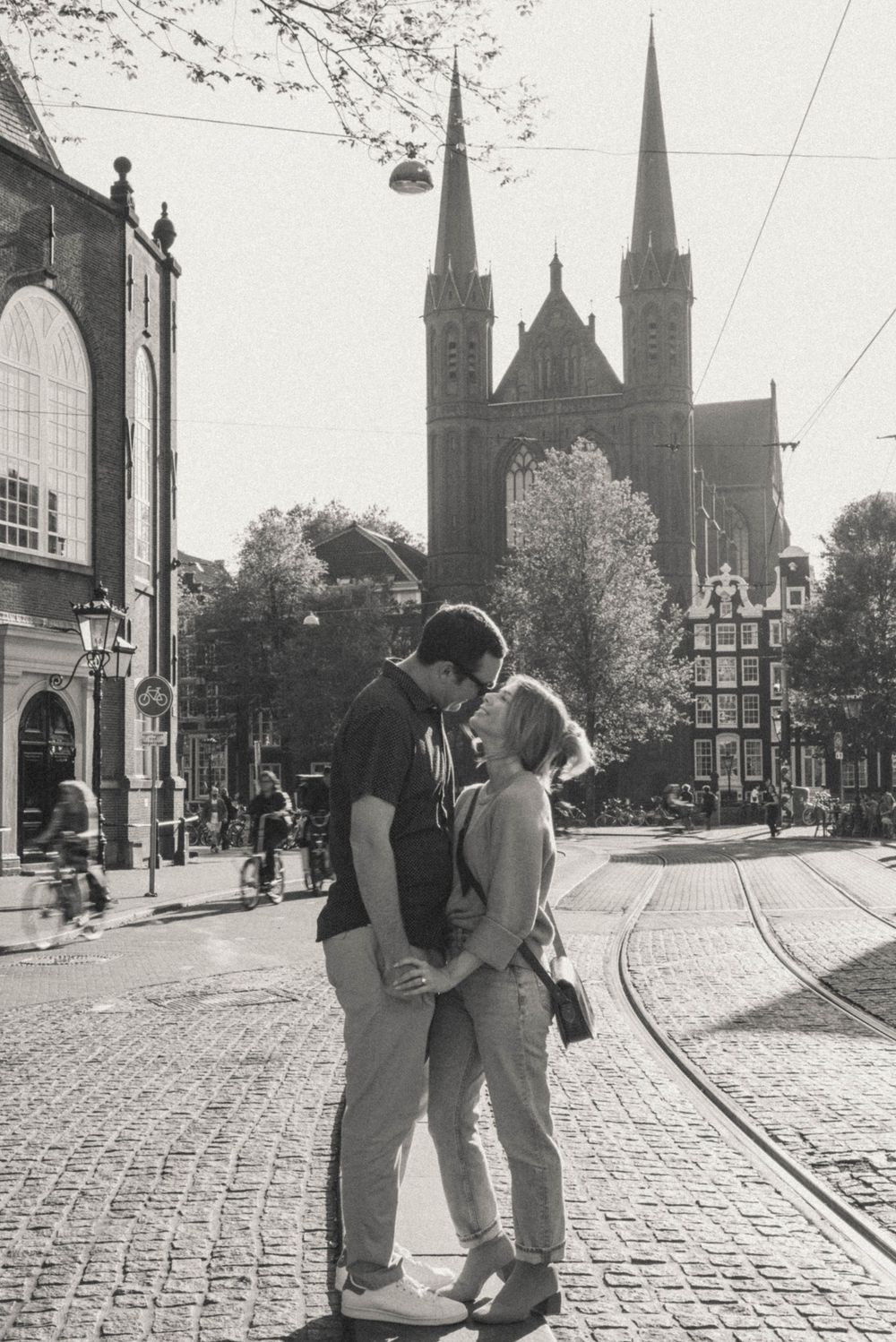 Black and white photo of couple on cobblestone street with gothic church spires in background.