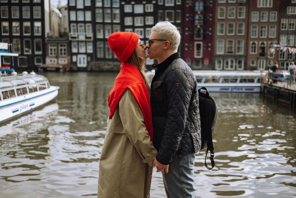 Couple in winter coats sharing tender moment along Amsterdam canal with historic buildings.
