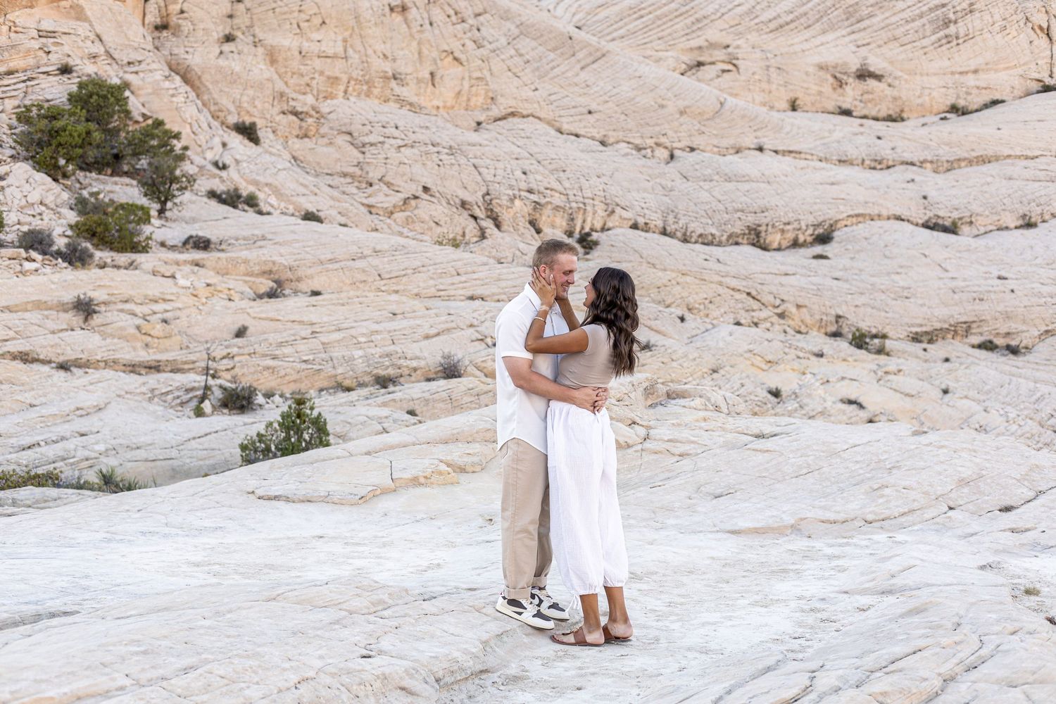 Cora Emilie Media -A couple embraces on white rock formations in a desert landscape.
