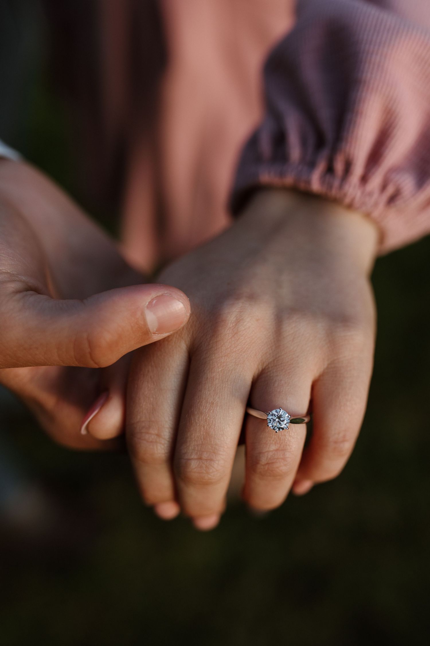 A close-up of hands showing off a sparkling diamond engagement ring against a soft background.