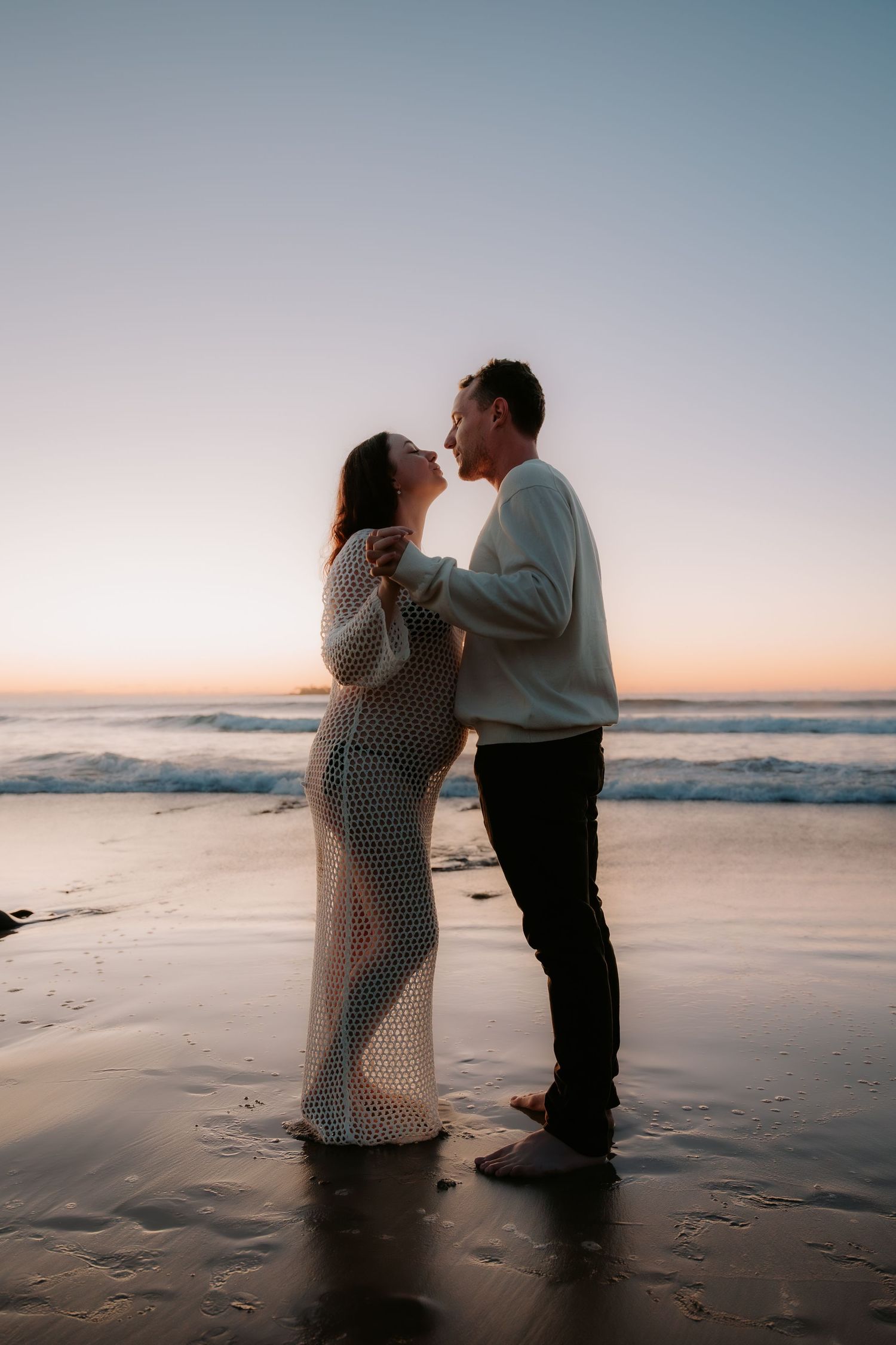 Romantic couple embracing on beach at sunset with waves in background.