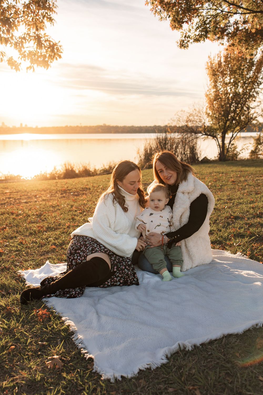 Sunset photoshoot by lake with white blanket and autumn trees in background.