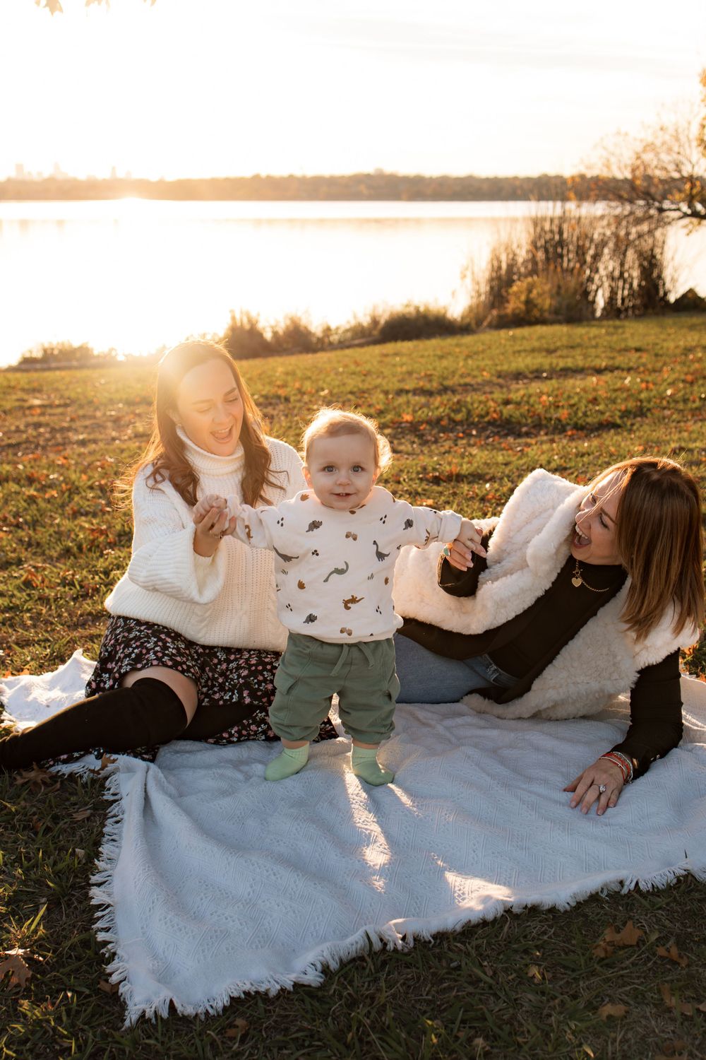 Family moment captured on white blanket by lake during golden hour.