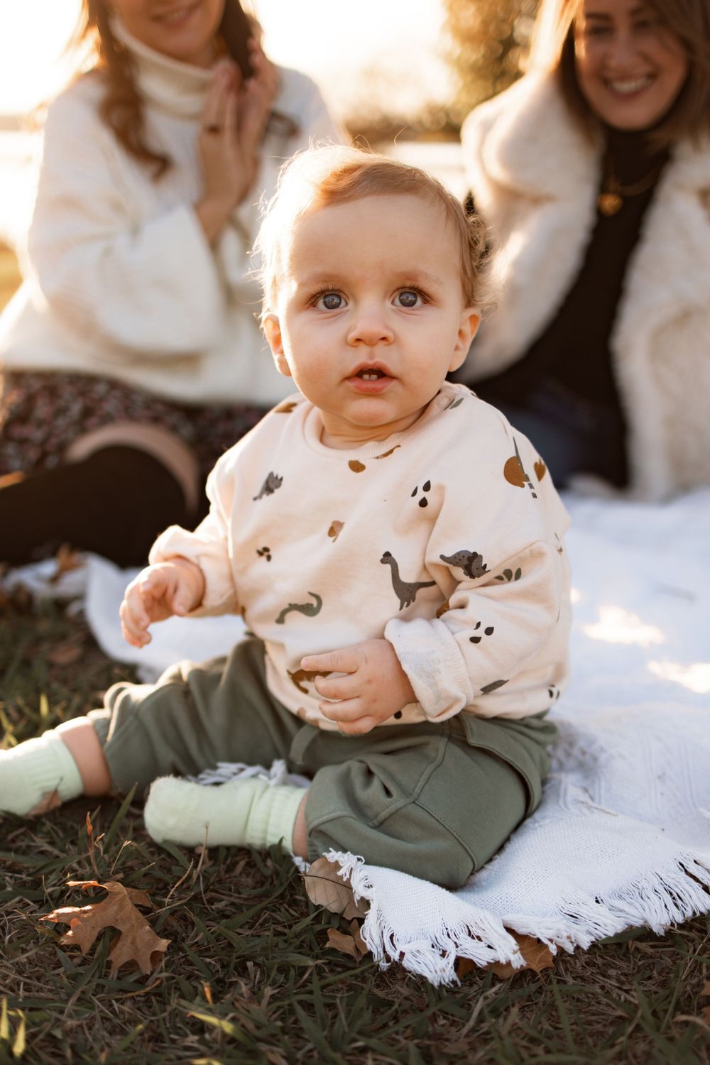 Toddler in animal print sweater sitting on white blanket during golden hour.
