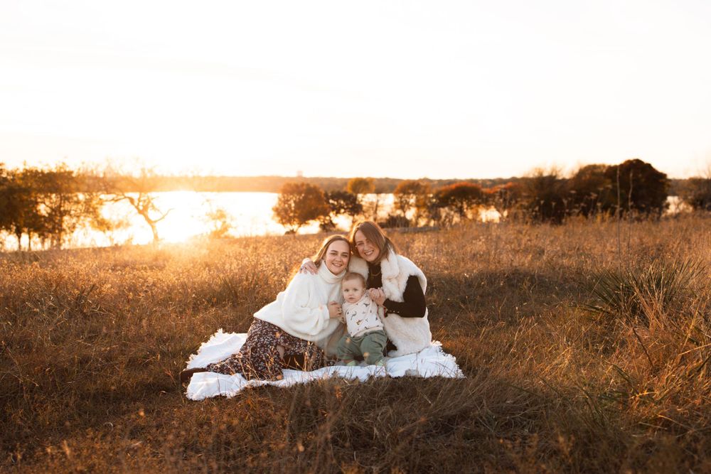 Sunset picnic scene with family sitting on white blanket near a lake.