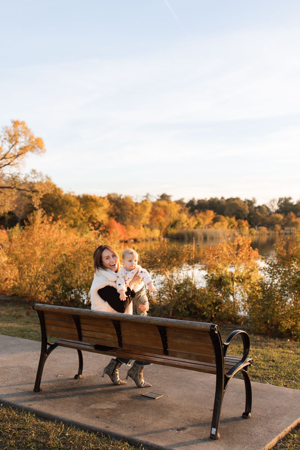 People sitting on park bench overlooking lake with autumn trees during sunset.