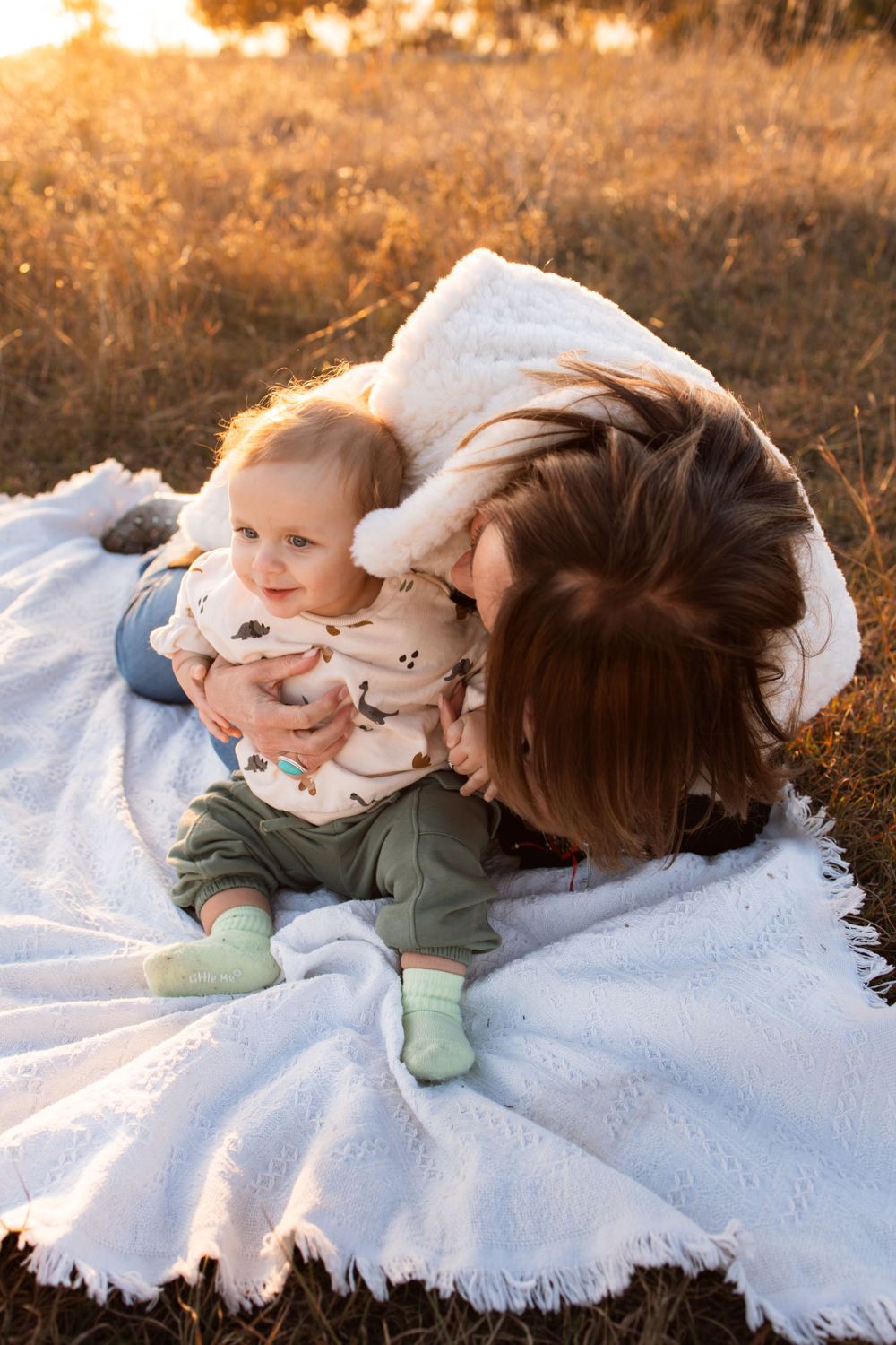 A tender moment captured on white blanket during golden hour outdoors.