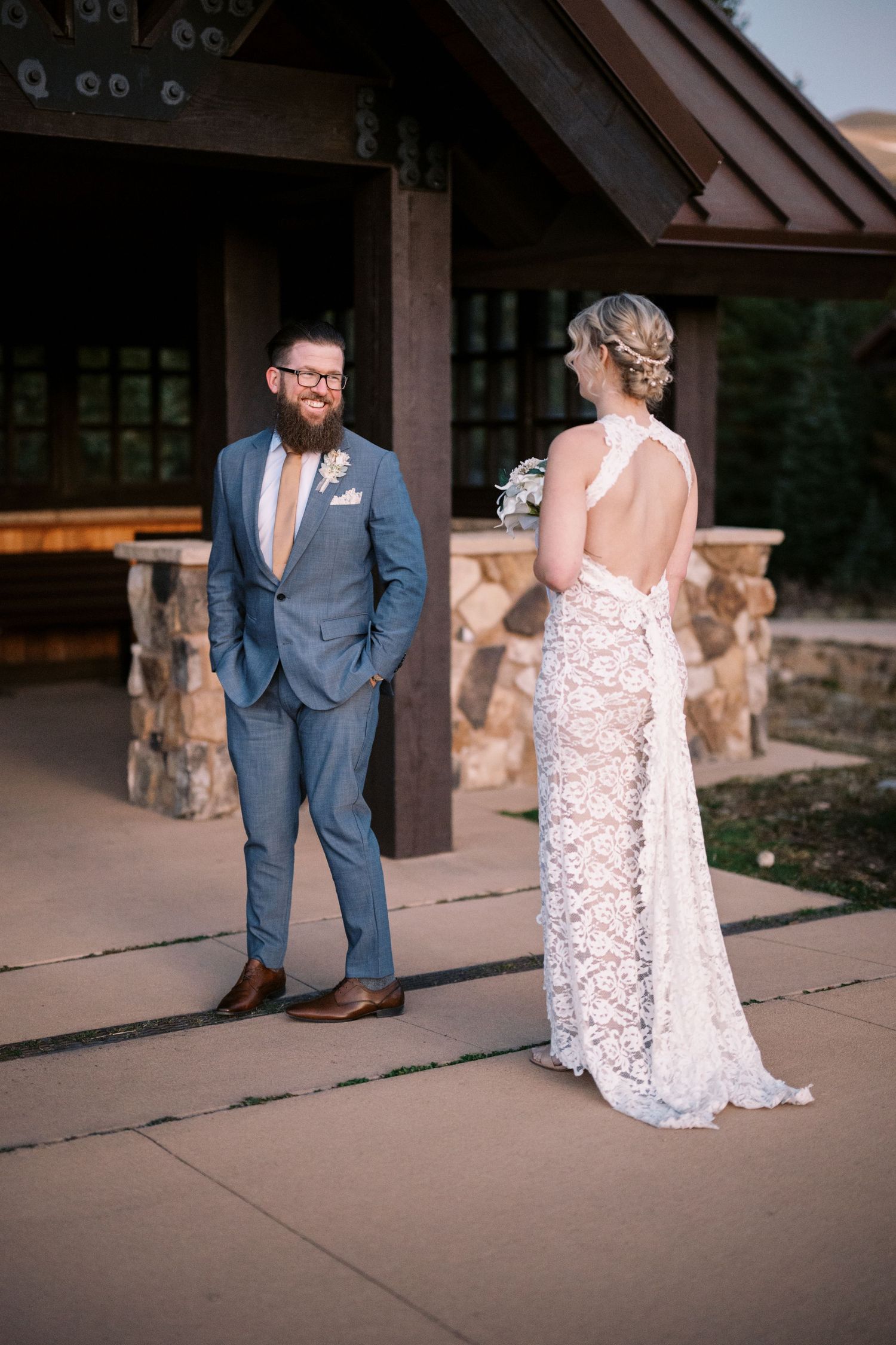 A couple shares a wedding day moment at their outdoor venue with a rustic stone and wood structure in the background.