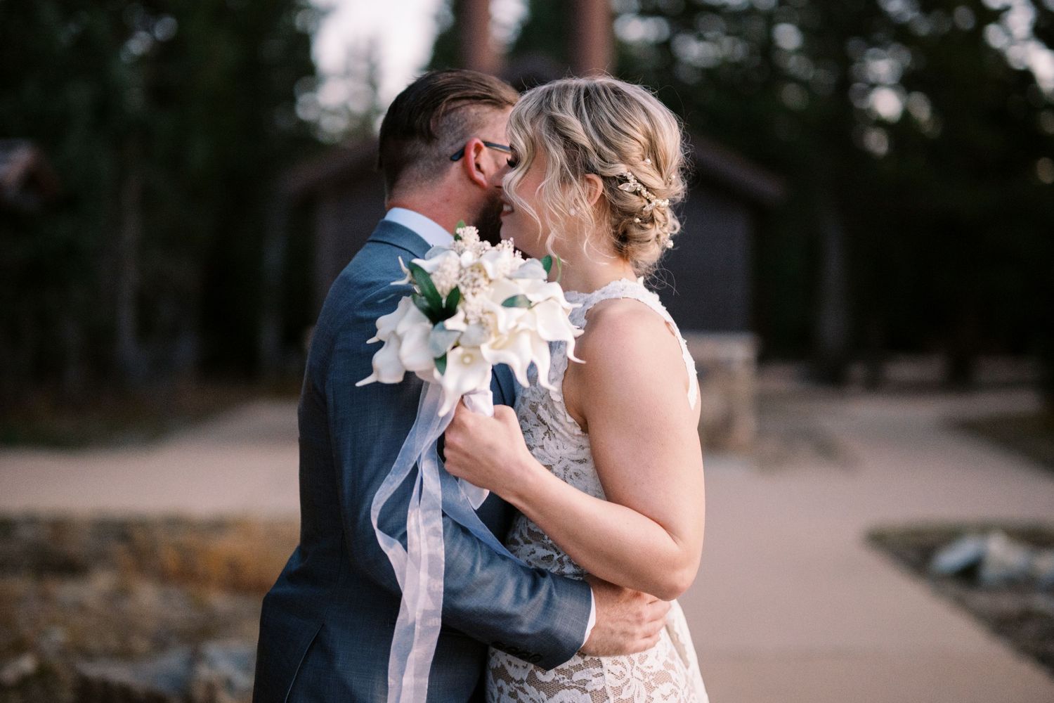 A couple shares a romantic moment at an outdoor wedding venue as sunshine filters through the trees.