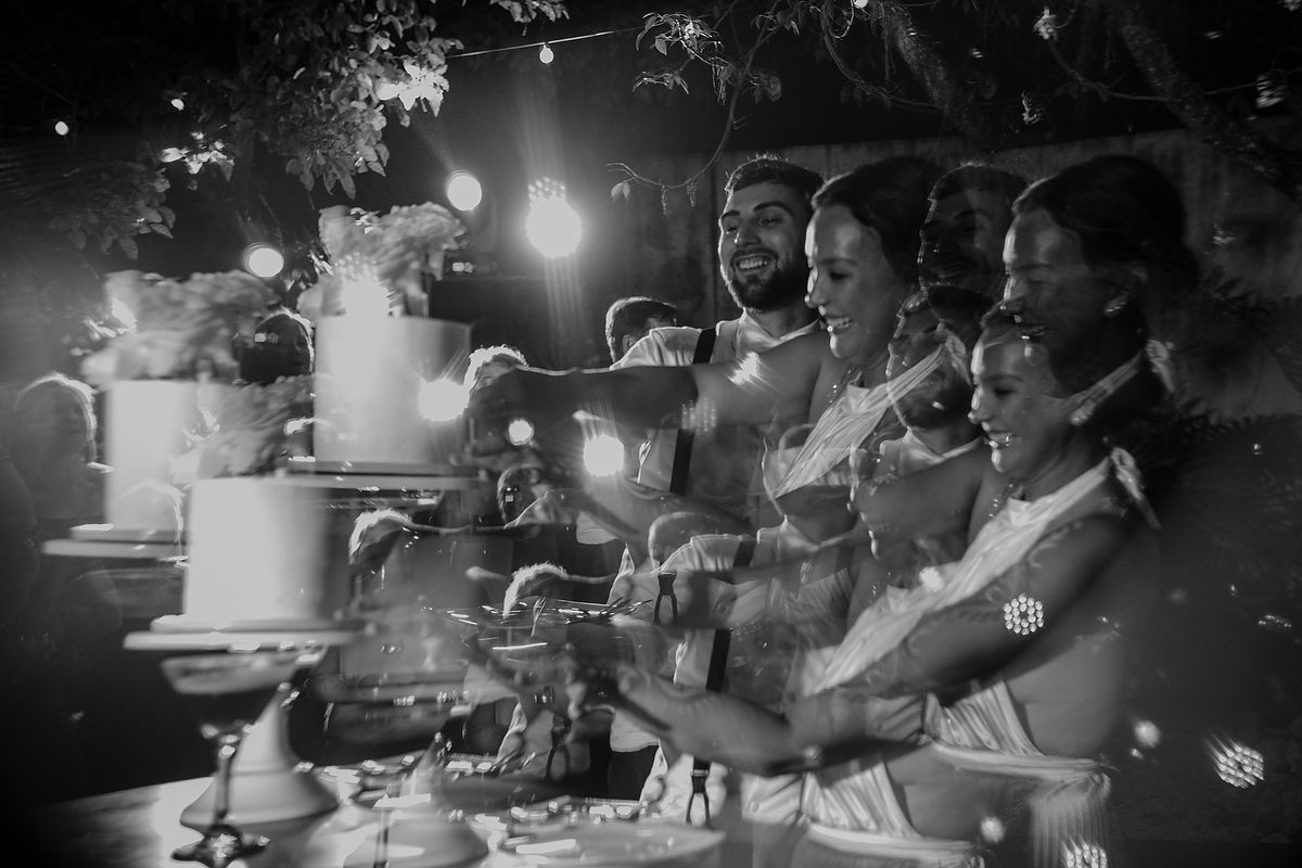 Black and white photo of a group celebrating around a wedding cake at an outdoor evening reception.