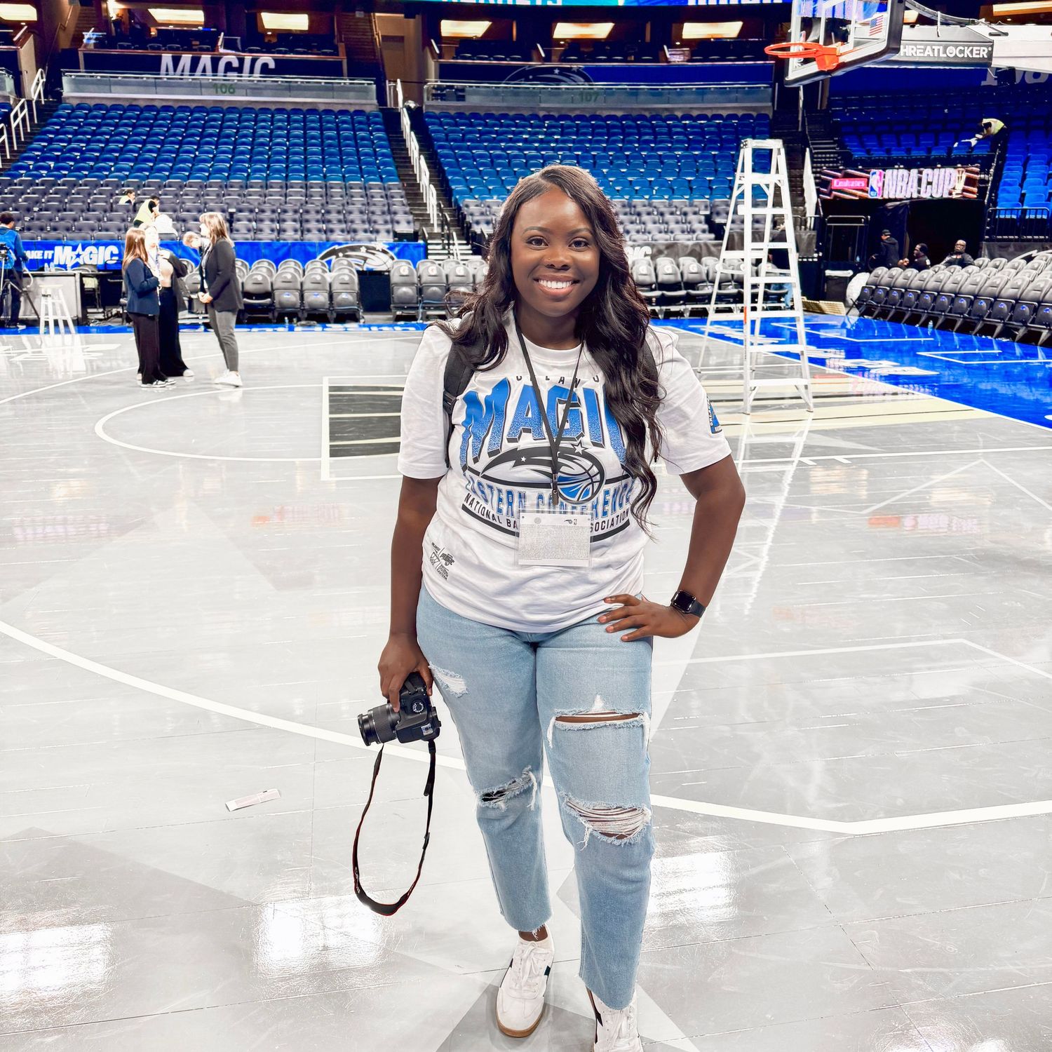 Person posing for photos on an empty basketball court in ripped jeans and white sneakers.