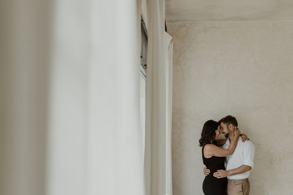 Couple sharing tender embrace against white wall in minimalist setting.