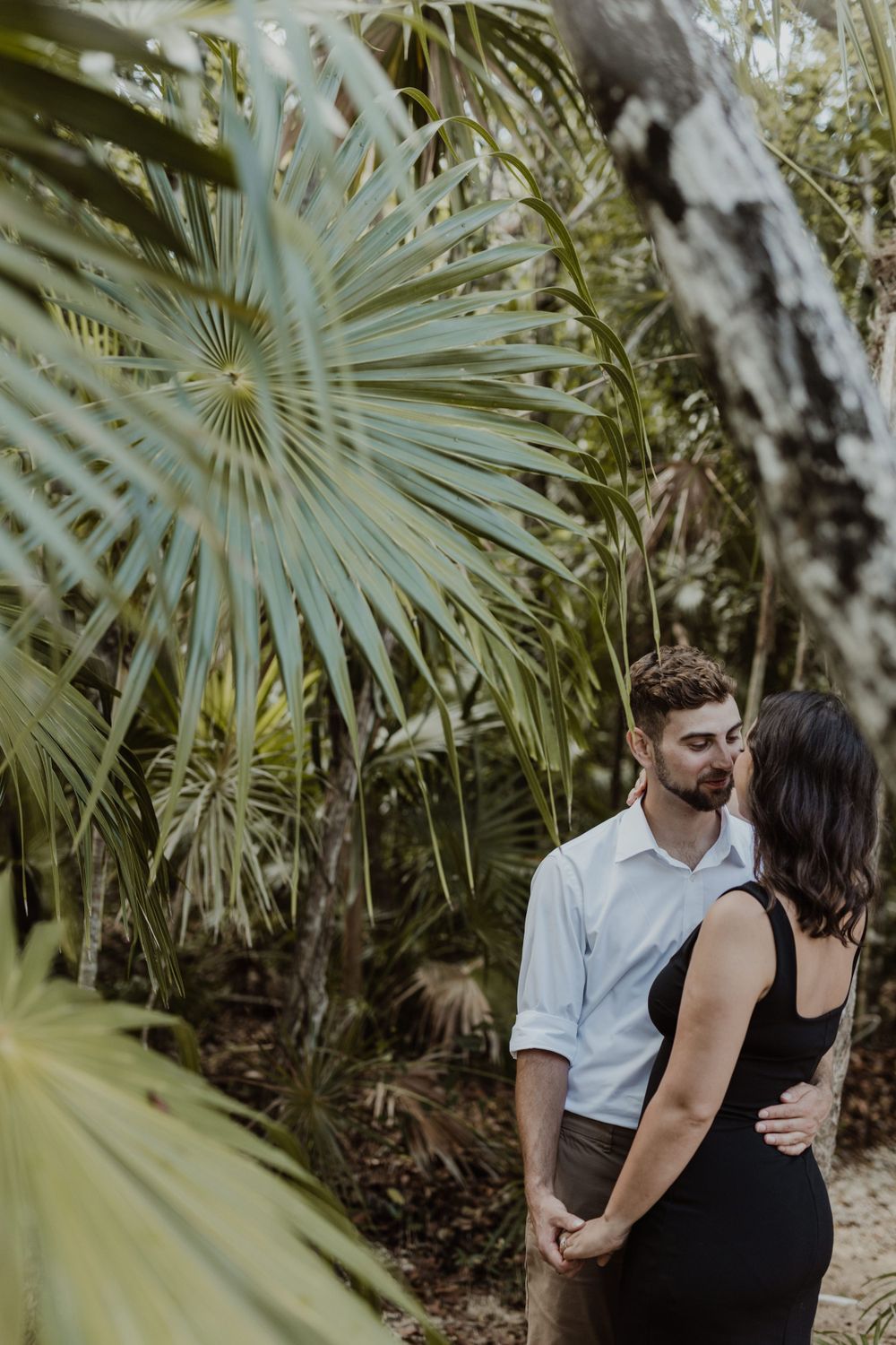 Romantic couple standing among tropical palm trees in natural setting.
