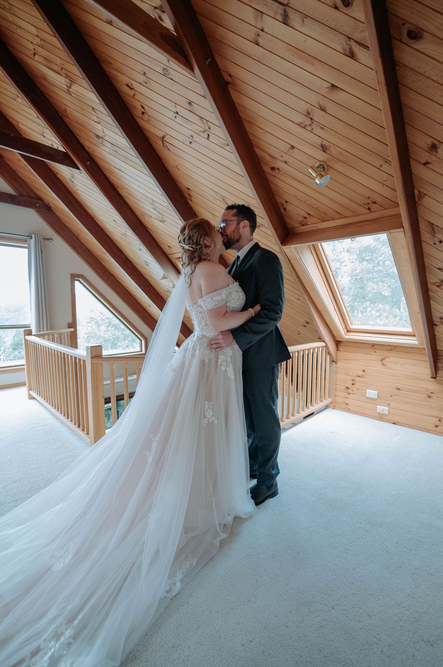 A romantic embrace between newlyweds in a sunlit A-frame cabin with vaulted wood ceilings.