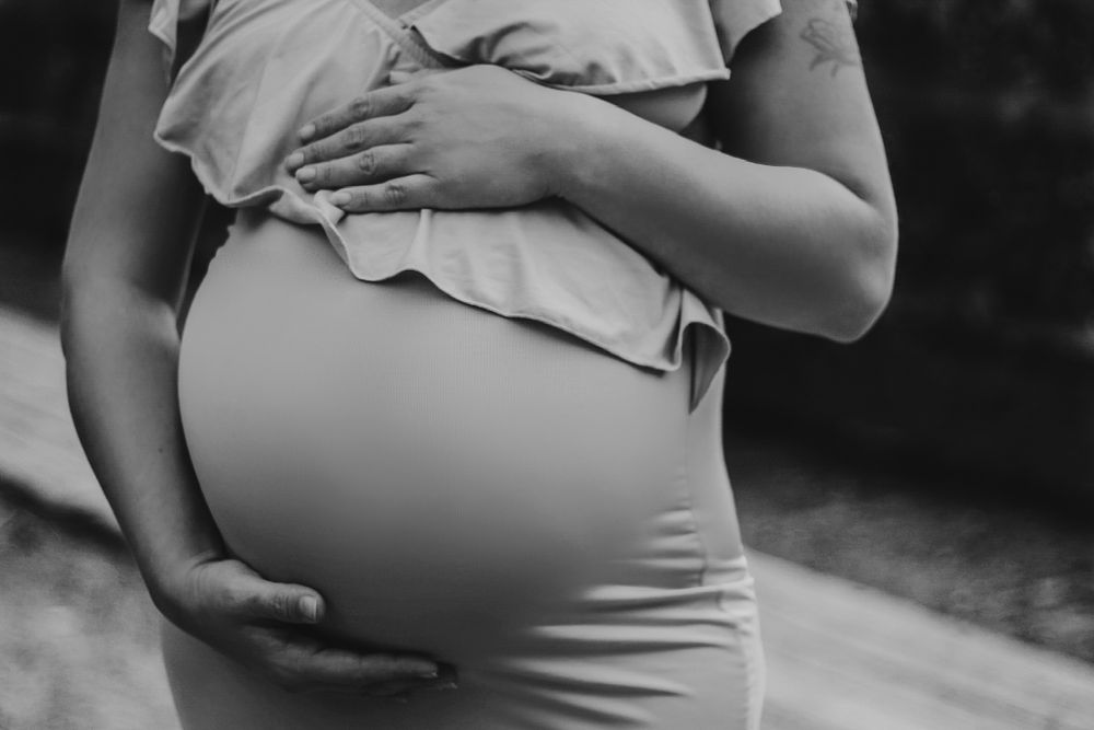 Black and white close-up of a pregnant woman cradling her baby bump with both hands.
