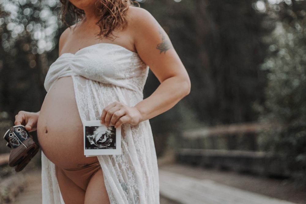 Close-up of pregnant woman holding ultrasound photo with visible baby bump and tattoo.