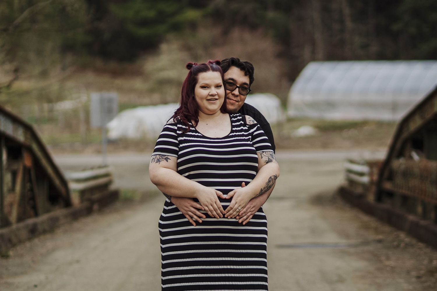 Couple posing on rustic bridge, hands cradling pregnant belly, during maternity shoot.