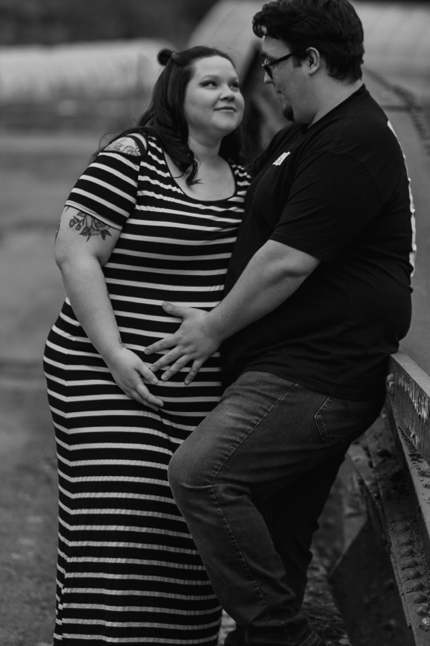 Black and white maternity photo of couple holding pregnant belly together outdoors.