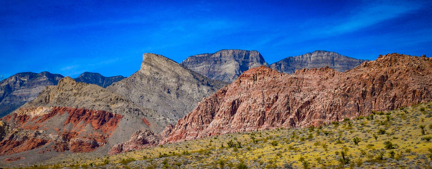 Panoramic view of rugged desert mountains with red rock formations under blue sky.