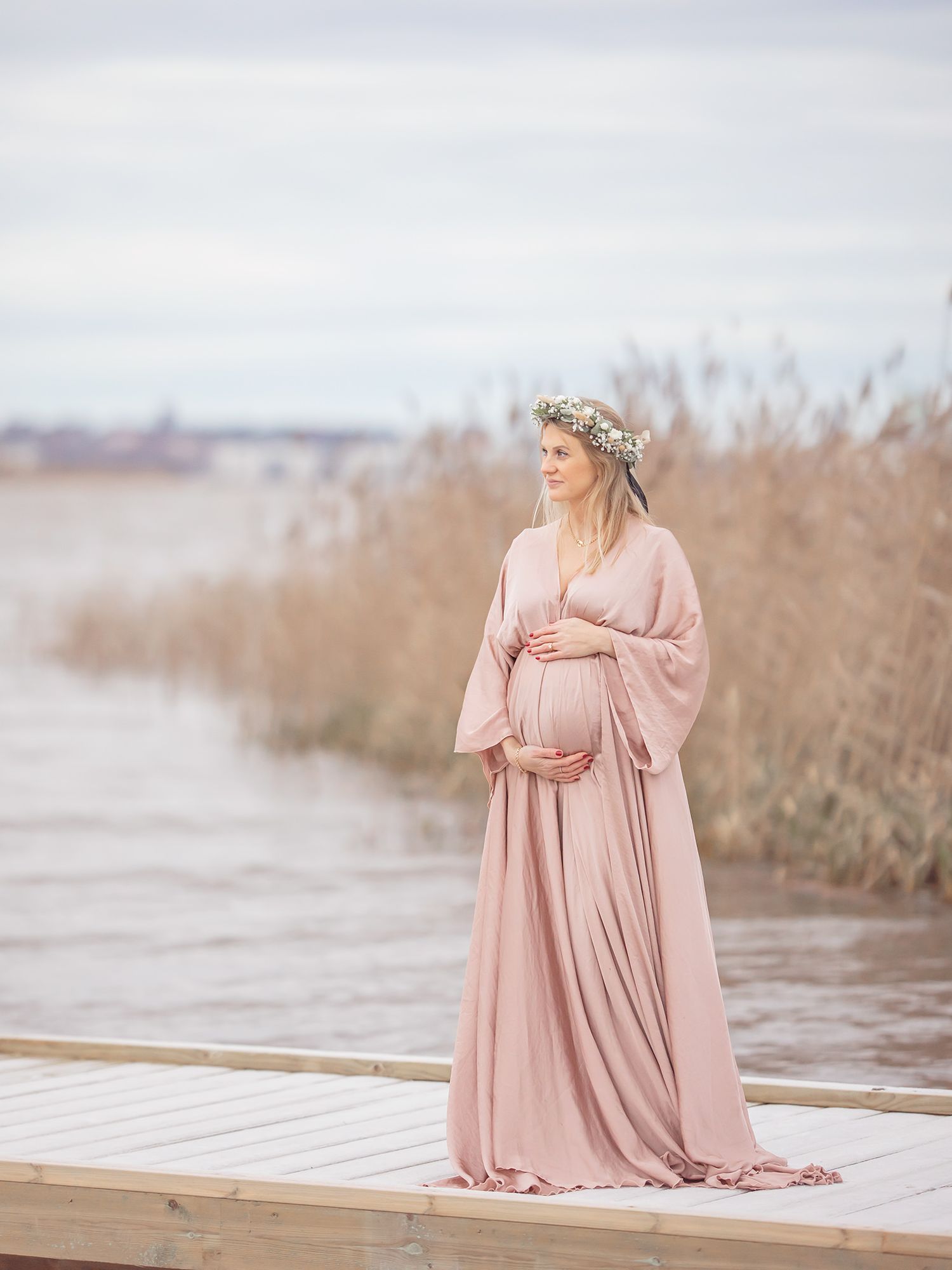 Gravid mamma på en brygga vid vattnet i satin gravidklänning , Gravidfotograf i Västerås, MemoriebyM.se, pastell