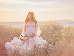 Gravid mamma står på sandstrand i motljus, Gravidfotografering i Västerås, goldehour, MemoriesbyM.se, pastell